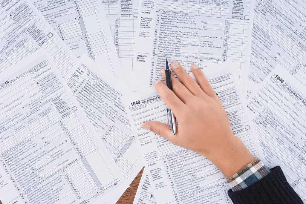 A man's hand on numerous IRS tax forms on a desk. Form 941 or Schedule H?