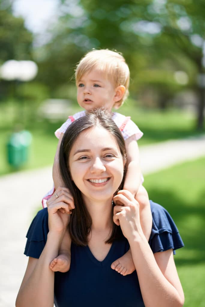 Smiling au pair carries a little girl on her shoulders. Close-up. High quality photo