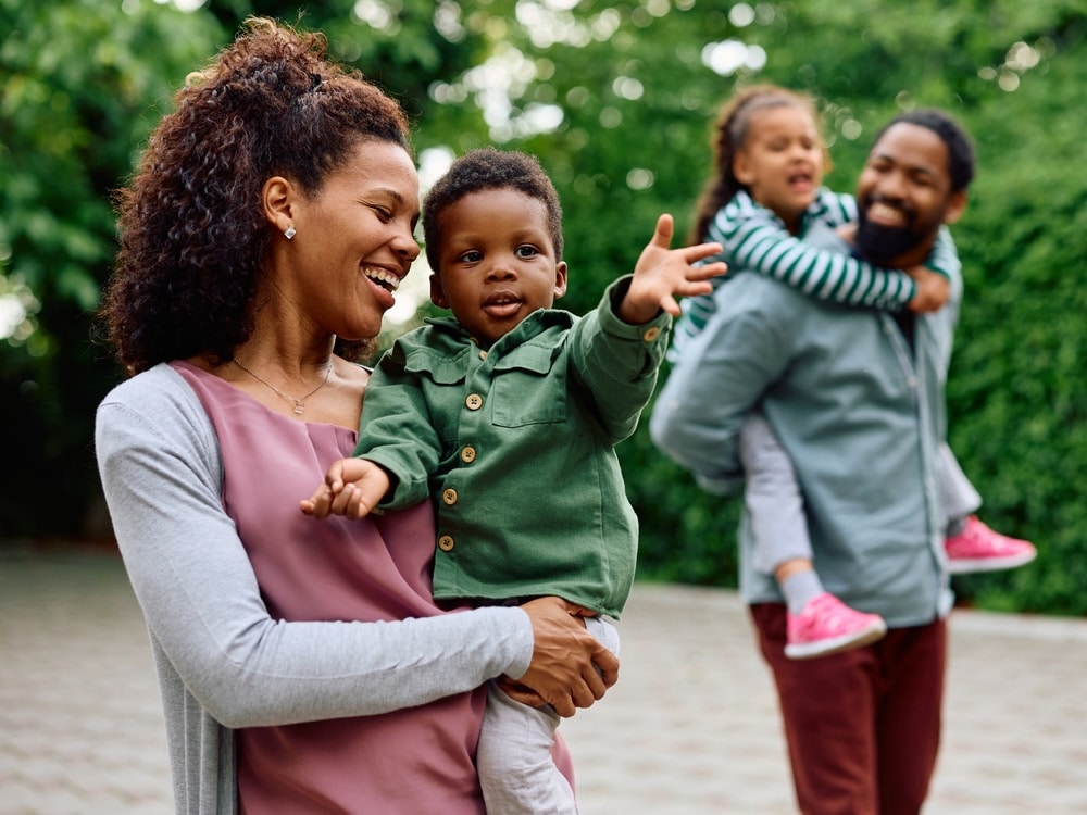 Happy woman holding her small son while walking outdoors. Father and daughter are in the background.