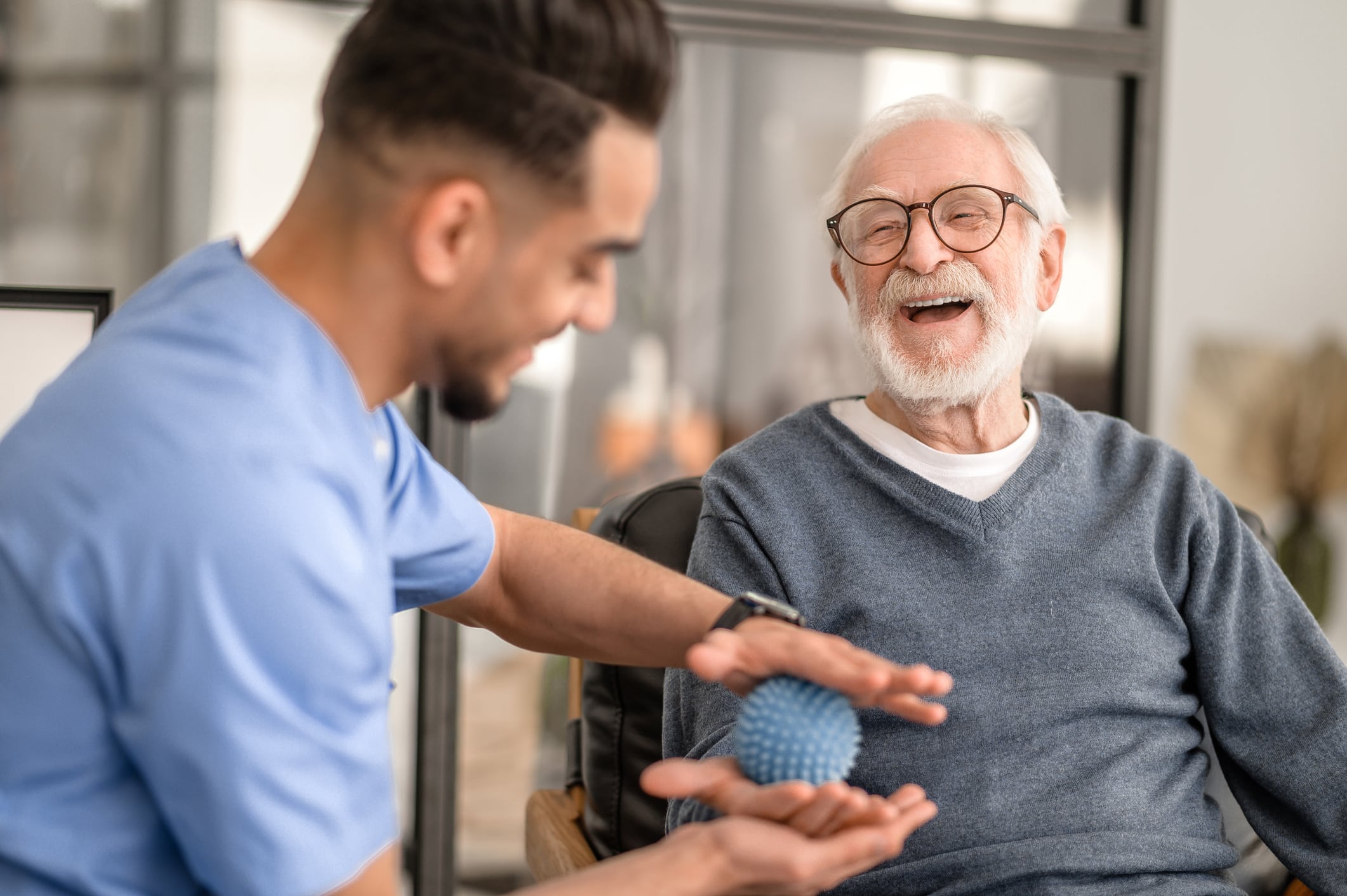 Joyous aged man undergoing a session of physical therapy conducted by an experienced rehabilitation doctor